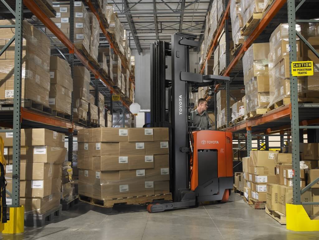 La carretilla elevadora que transporta un gran palé de muchas cajas de cartón gira en un pasillo estrecho de un almacén 