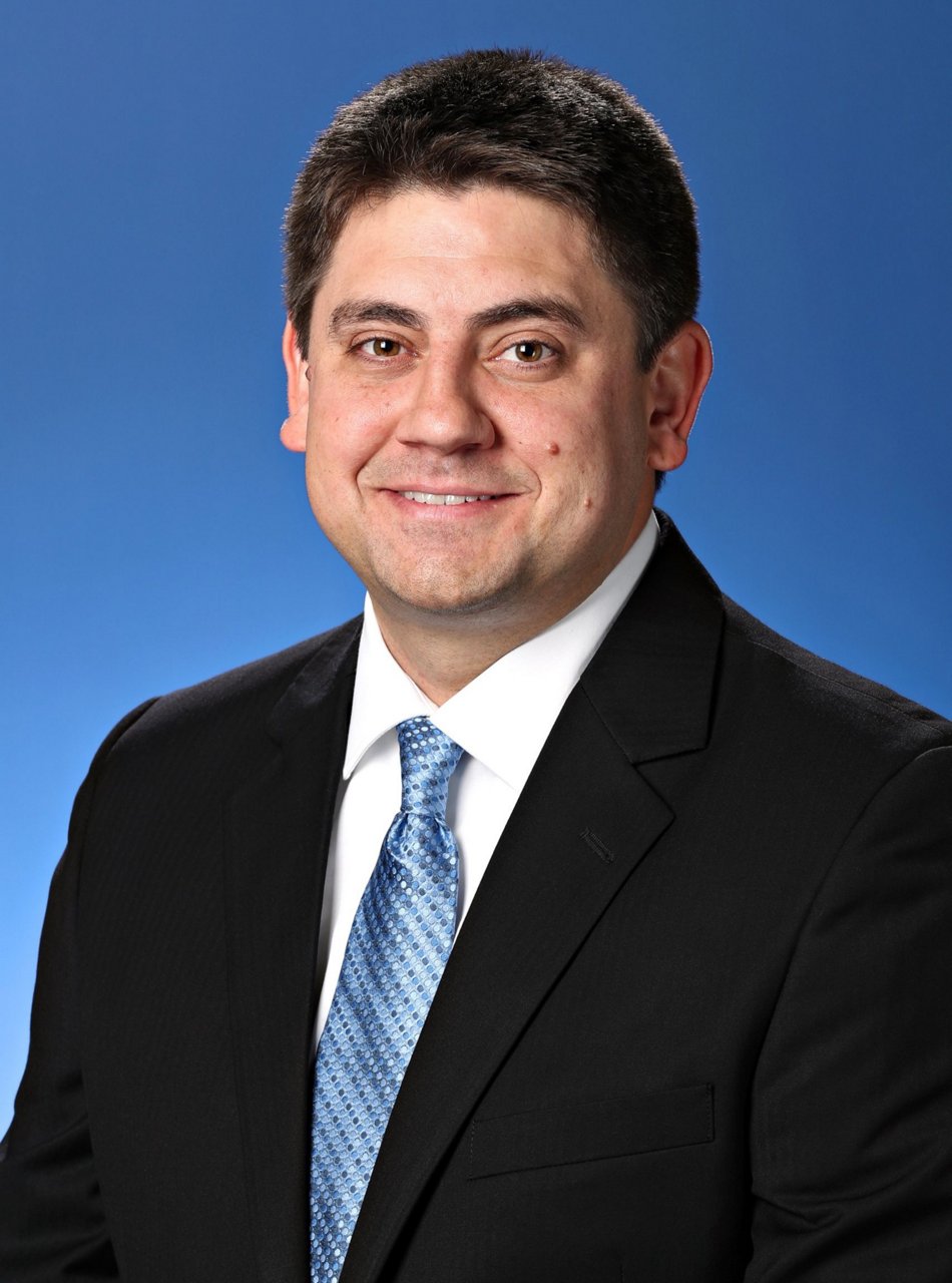 Portrait professionnel d’un homme blanc portant une veste de costume noire et une cravate bleue sur fond bleu