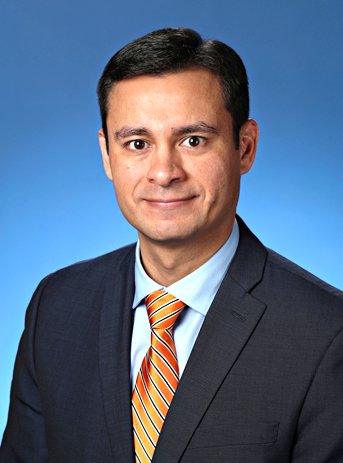 Retrato profesional de un hombre blanco con un traje de chaqueta negro y corbata naranja sobre un fondo azul