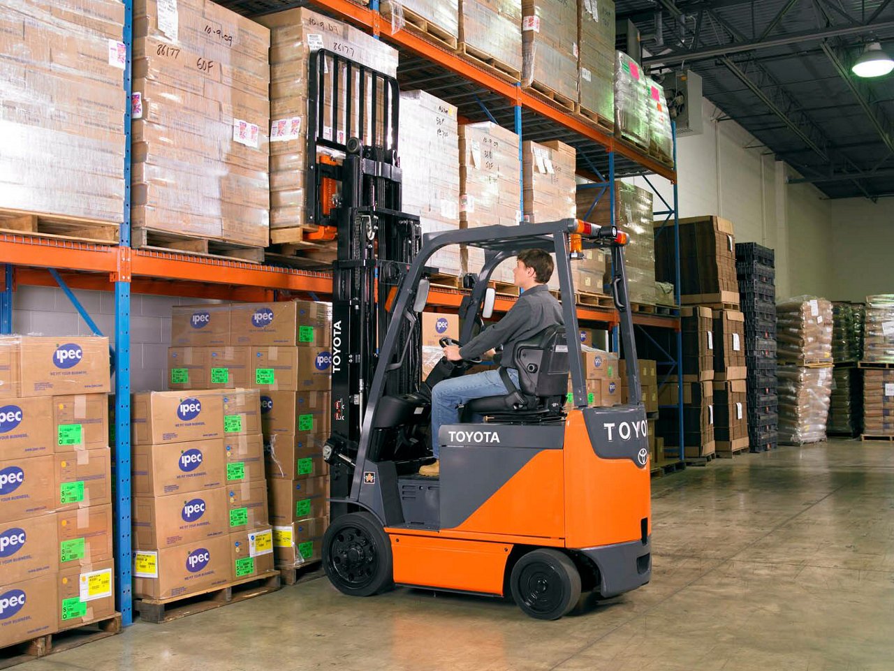 Man driving core electric forklift in warehouse, loading cardboard boxes onto a shelf.