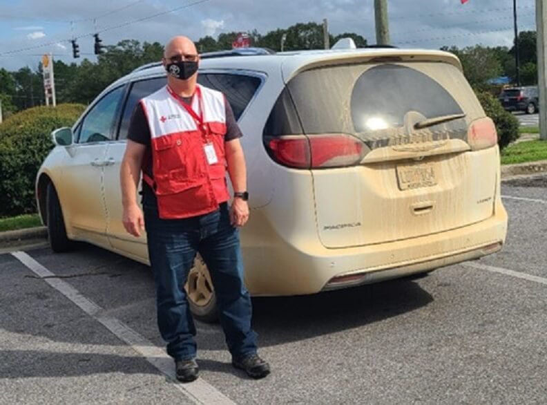 Un hombre llamado Dean Stewart parado afuera de una camioneta blanca en un estacionamiento 