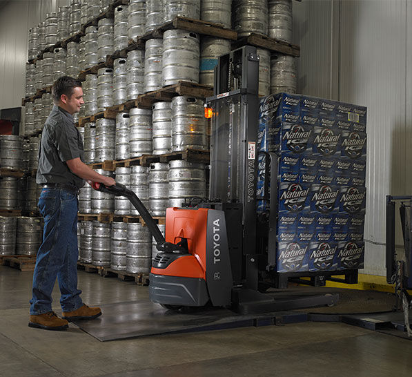 A man using an electric walkie in a beverage storage warehouse to carry many boxes of natural ice.