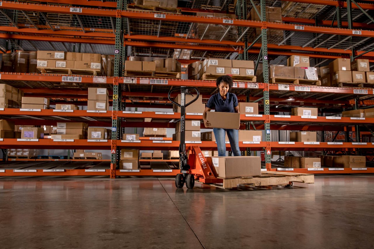 A woman loading a Toyota pallet truck with cardboard boxes in a warehouse 