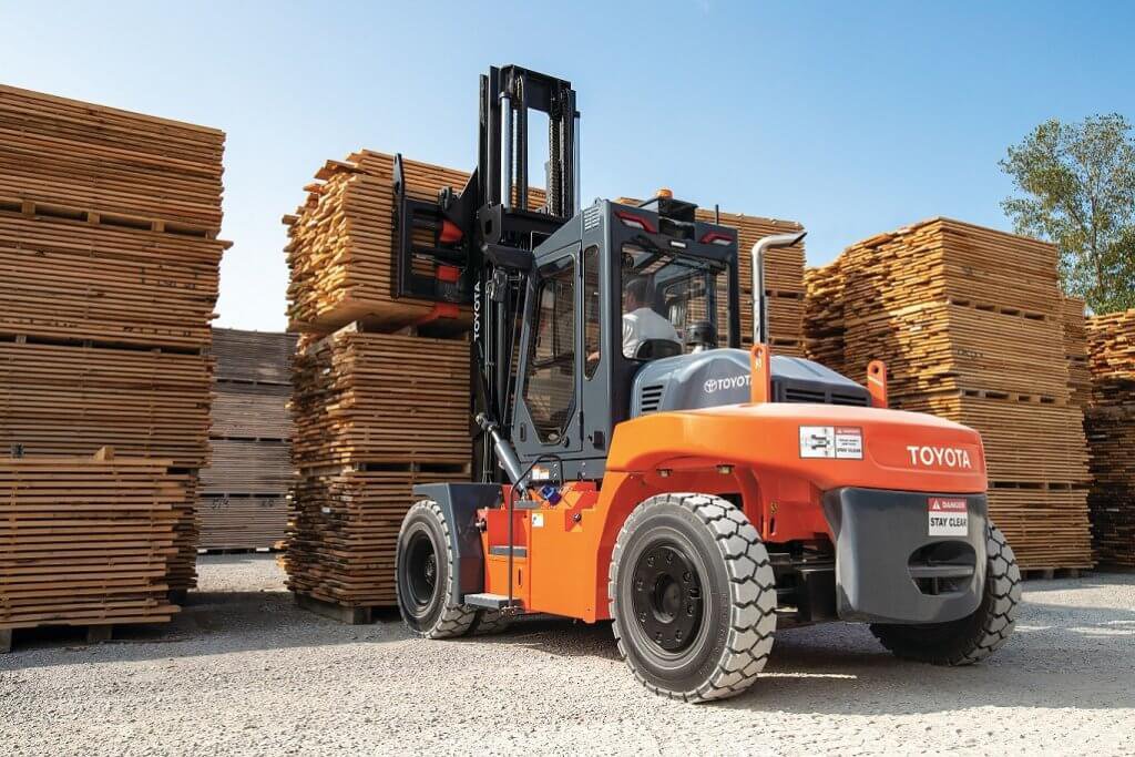 Large Capacity Core IC Pneumatic Forklift lifting wooden pallets from a tall stack outside in a wood storage lot