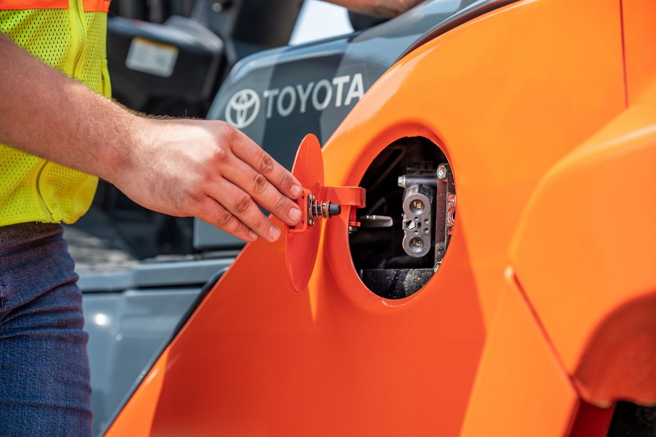 Homme ouvrant le compartiment pour recharger un grand chariot élévateur intégré Toyota orange