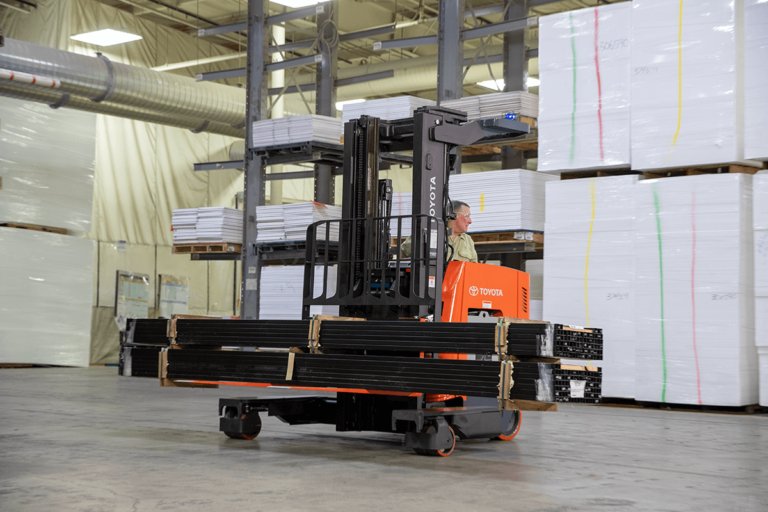 Multidirectional Reach Truck driving through warehouse while carrying two bundles of pipes