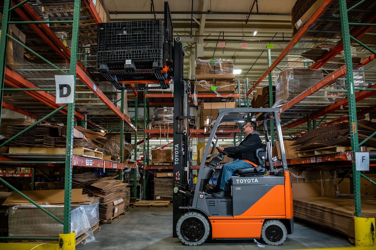 Man driving a forklift in the warehouse to pick boxes from a high shelf