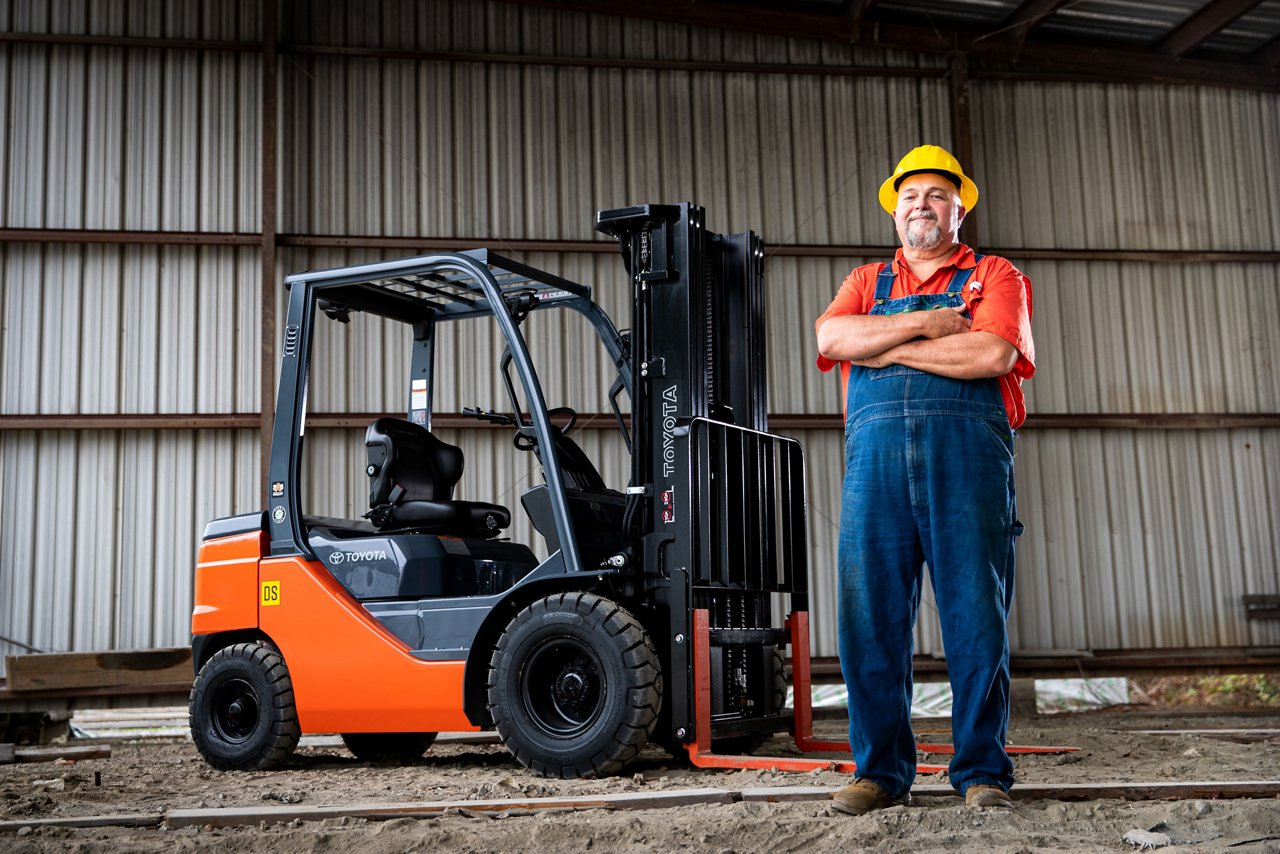 Man with hard hat in warehouse, smiling and crossing his arms, in front of Toyota Core IC Pneumatic Forklift in warehouse