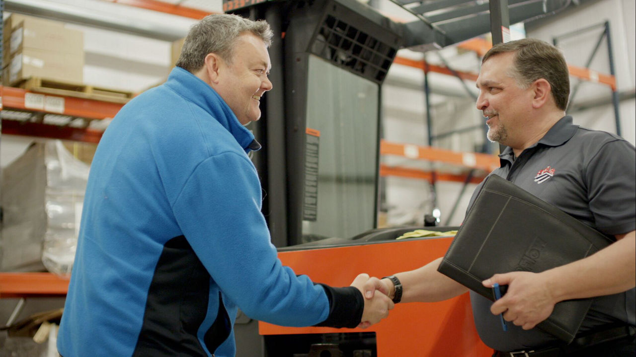 Two men shake hands in a warehouse with a Toyota forklift in the background 