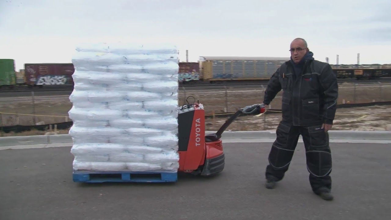 Un hombre usa un Walkie eléctrico Toyota para transportar varias bolsas de hielo en un lote de carga al aire libre 