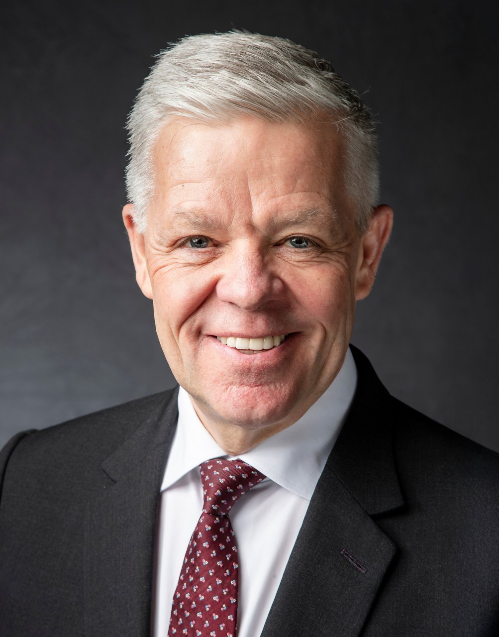 Sam Coles headshot with a black suit and burgundy tie