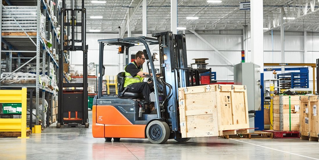 Un hombre conduce una carretilla elevadora Toyota que transporta una caja de madera por el almacén 