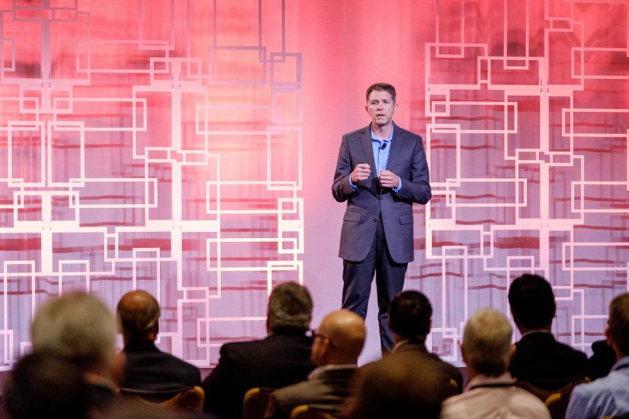 Man speaking to crowd on stage at a conference 