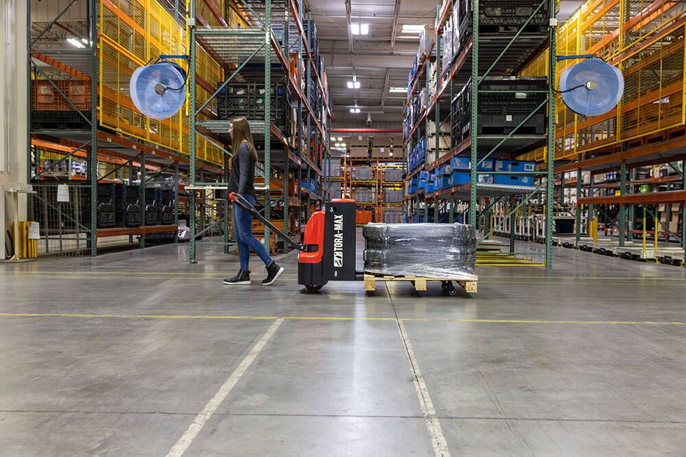 Woman using Tora Max Electric Walkie to carry 2 large tires across warehouse 