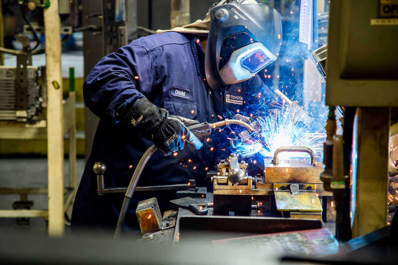 toyota welding associate with hard hat on welding a piece of equipment