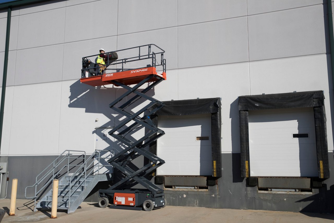 Man using a Toyota Scissor Lift outside along warehouse wall