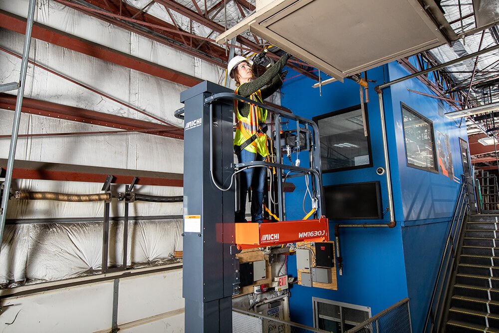 Mujer que usa un elevador de mástil vertical para ajustar el accesorio de techo en el almacén