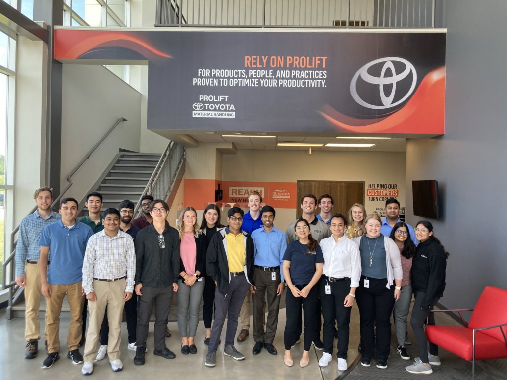 21 pasantes sonrientes de Toyota Material Handling tomando una foto grupal en el vestíbulo de un concesionario Prolift