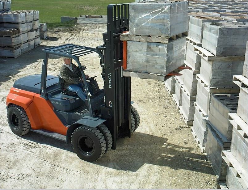 Hombre conduciendo una carretilla elevadora neumática Core IC de alta capacidad y levantando dos paletas de material en un lote al aire libre. 