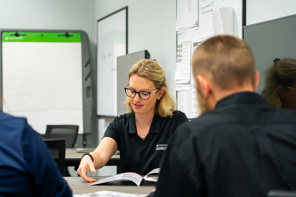 women with glasses sitting at desk with employees looking at pamphlet