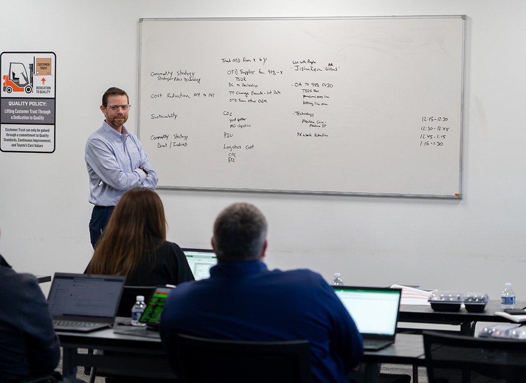 tmh associate stands next to a white board teaching, as three tmh associates sit at desks watching