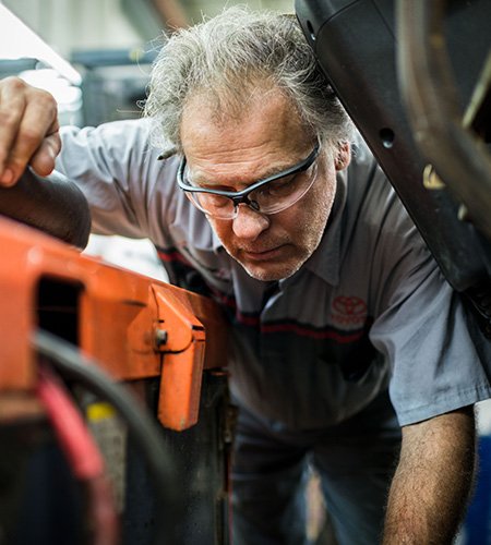 Un technicien de chariot élévateur Toyota porte des lunettes et regarde dans un chariot élévateur