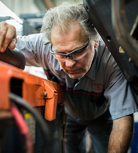 Técnico de montacargas de Toyota con gafas y mirando dentro de la carretilla elevadora